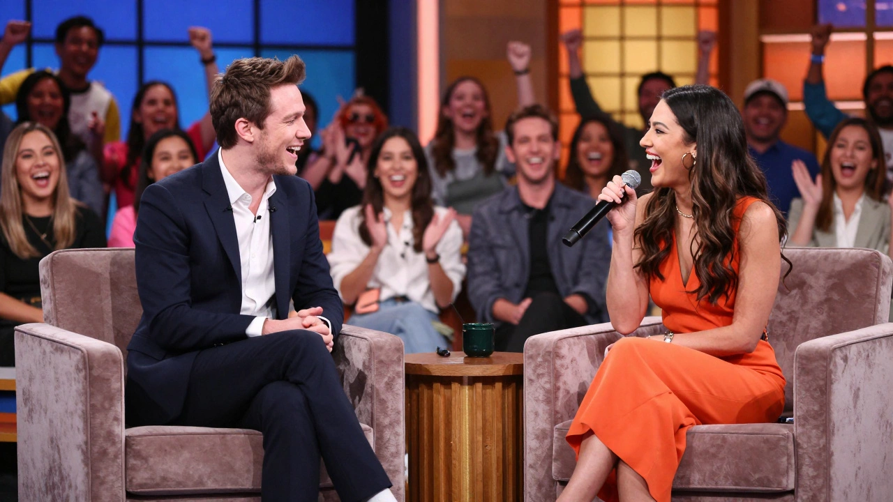 A charismatic host and celebrity guest laughing on a brightly lit comedy talk show set.